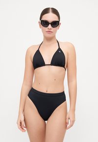 Svart bikiniset med en trekantet topp med justerbare stropper og høytlivde bunn. Glatt stoff og minimalistisk design. Svart solbriller.