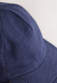 Gorra azul marino con textura de tela suave, corona redondeada, visera curva y costuras sutiles. El diseño presenta un aspecto limpio y minimalista.