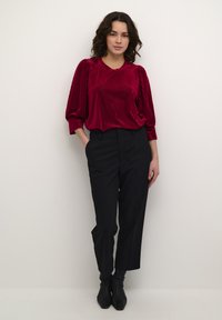Blusa roja con pliegues y escote redondo, pantalones negros de corte ajustado y botines negros. Textura suave con un corte relajado.