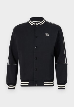 Fekete pulóverdzseki fehér csíkos bordás gallérral és mandzsettával. Gombos záródású, a bal felső részen logóval ellátott, puha anyagból készült.