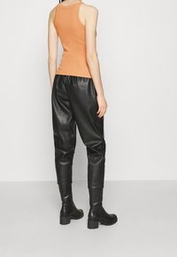 Top arancione senza maniche con un design aderente, abbinato a pantaloni in ecopelle neri a vita alta e stivali neri con tacco al ginocchio.