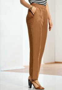 Bruine, elastische taillebroek met zijzakken, met een gladde textuur en een taps toelopend ontwerp, gecombineerd met tan hoge hakken sandalen.