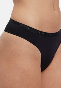 Zwarte string met een zachte elastische tailleband waarop de merknaam "FALKE" subtiel en contrasterend is gedrukt. Gladde textuur.