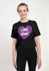 Camiseta negra con un diseño de corazón púrpura que incluye el texto "CARE BEARS" en blanco y rayas de colores. Mangas cortas y ajuste estándar.