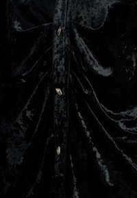 Camisa de terciopelo negro con una textura suave, frunces en la parte frontal y botones en tono dorado a lo largo de la tapeta.