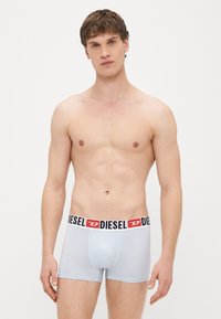 Gaiši zilas bokserbikses no elastīga auduma ar melnu jostu, uz kuras ir sarkans un balts "DIESEL" uzraksts.