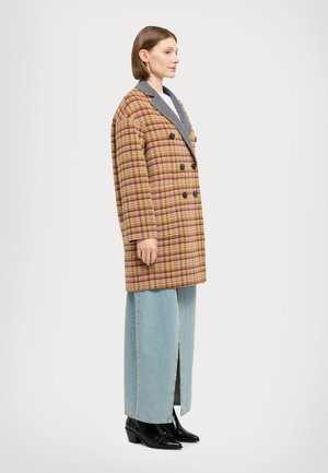 Double-breasted coat in brown and pink plaid, with a grey collar, paired with light blue wide-leg jeans and black heeled boots.