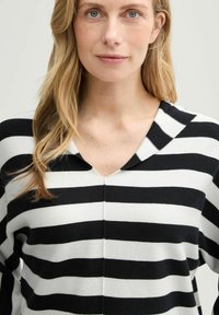 Pull à rayures noir et blanc avec un col en V et une texture douce. Les rayures sont uniformément espacées, créant un motif audacieux.