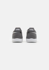 Zapatillas deportivas grises con parte superior de tela texturizada, detalles en blanco y el texto "KING" en el talón. Presenta una suela blanca con patrón para mayor tracción.