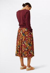 Bordeaux sweatshirt gecombineerd met een bloemenpatroon, knielange rok in warme tinten van rood, oranje en groen. Witte sneakers met oranje strepen.