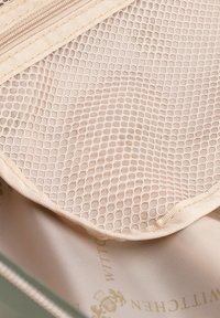 Poche en maille beige clair avec un motif hexagonal, dotée d'une fermeture éclair lisse et d'une base en tissu vert doux et brillant avec un logo subtile.