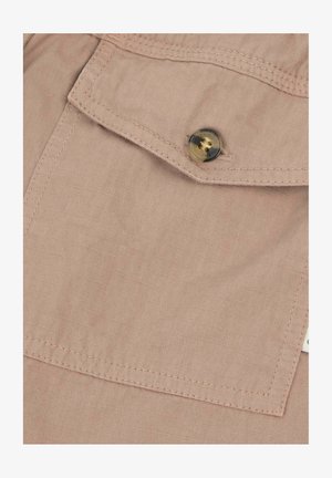 Primo piano di una tasca in tessuto beige con patta chiusa da un bottone rotondo bicolore e dettagli di cuciture visibili.