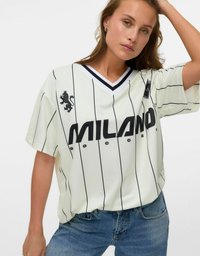 Vit kortärmad fotbollströja med svarta vertikala ränder, som har en svart lejonlogotyp och texten "MILANO" över framsidan.