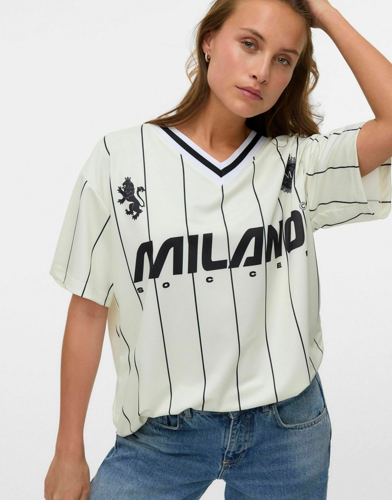 Vit kortärmad fotbollströja med svarta vertikala ränder, som har en svart lejonlogotyp och texten "MILANO" över framsidan.