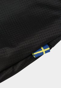 Musta kangasrasia, jossa on teksturoitu pinta. Pienen tarran siniset ja keltaiset ristikkäisviivat erottuvat kehyksestä.