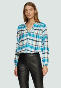 Blaue und weiße karierte Bluse mit langen Ärmeln und V-Ausschnitt, kombiniert mit schwarzen, hoch taillierten Lederhosen.