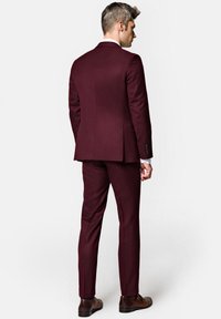 Bordowy garnitur o dopasowanym kroju, z pojedynczym rozporkiem z tyłu, gładką fakturą oraz brązowymi skórzanymi butami.