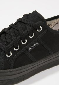 Sneaker nera in tela con lacci neri, occhielli argentati e un piccolo marchio "victoria" sul lato vicino alla suola.