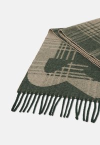 Skládaný zeleno-beige kostkovaný vlněný šál s třásněmi na okrajích na bílém pozadí.