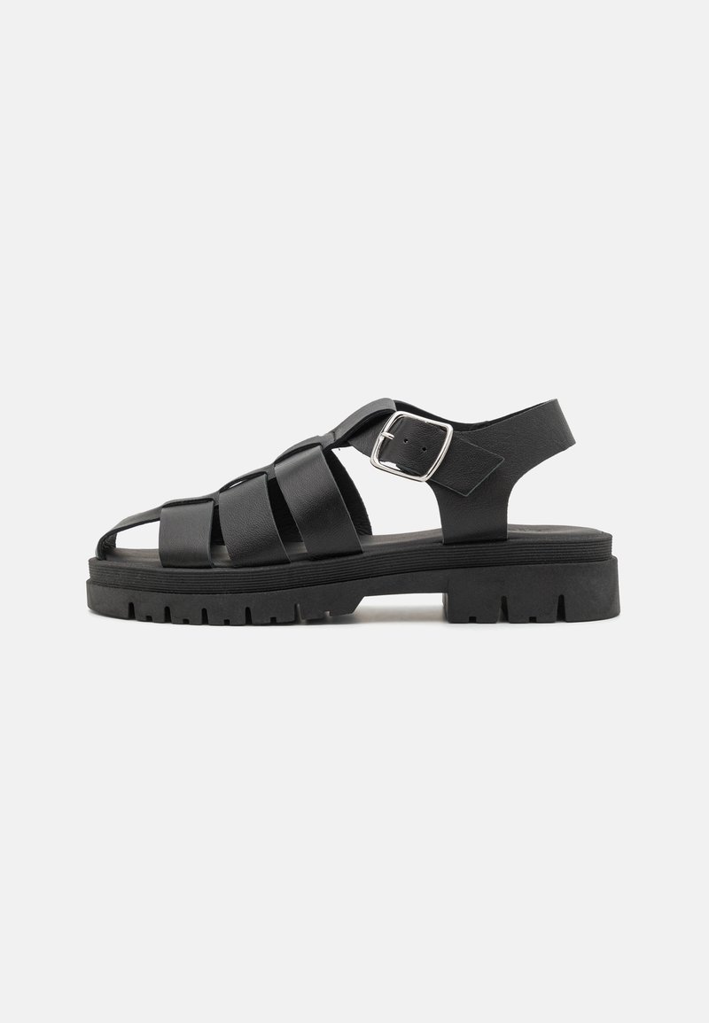 Black leather sandal with wide straps, open toe, adjustable ankle strap, and textured rubber sole. Chunky platform design for stability.