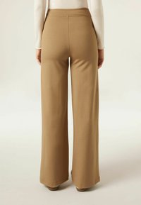 Pantalons larges beige en tissu doux, avec une taille haute et une coupe décontractée, finis par un ourlet net.