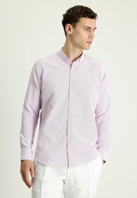 Camisa de botones de color rosa claro en tejido texturizado, con cuello, mangas largas y dobladillo recto. Los botones son pálidos y sutiles.