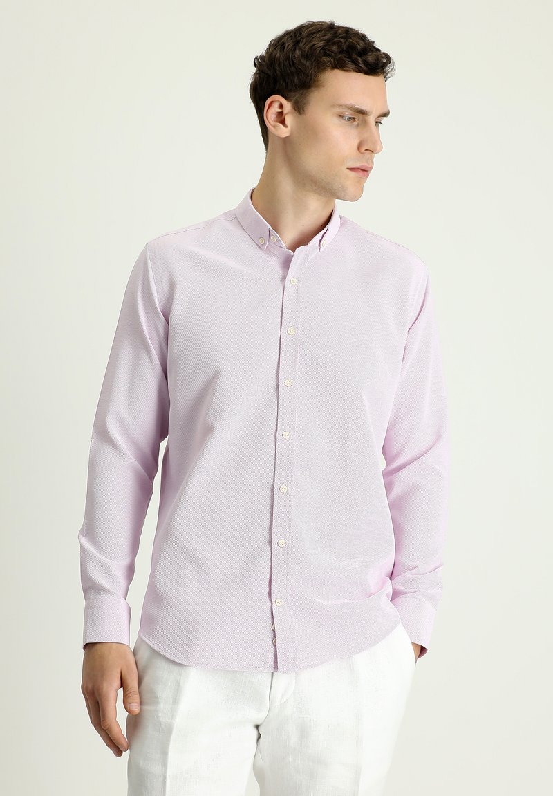 Camisa de botones de color rosa claro en tejido texturizado, con cuello, mangas largas y dobladillo recto. Los botones son pálidos y sutiles.