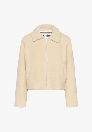 Īsā jaka ar rāvējslēdzēja aizdari priekšpusē, krēmkrāsas mākslīgā kažokāda ar mīkstu tekstūru, ar smailu apkakli un sānu kabatām. Raksturs ir vienkāršs, bez rotājumiem.