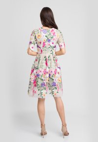 Sukienka w kwiaty z krótkimi rękawami, beżowa baza i żywe wielokolorowe hafty. Posiada dopasowany gorset i rozkloszowaną spódnicę.