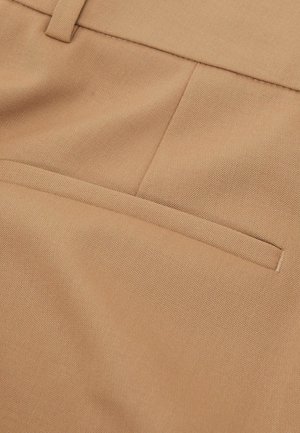 Gros plan sur un tissu beige présentant une surface texturée, avec une seule poche arrière et des détails de couture soignés.