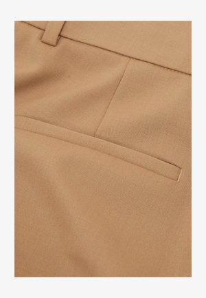 Gros plan sur un tissu beige présentant une surface texturée, avec une seule poche arrière et des détails de couture soignés.