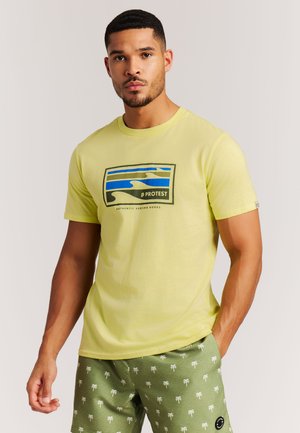 Felgele t-shirt met een grafische print van blauwe en groene golven, ronde hals, standaard pasvorm. Gecombineerd met groene shorts versierd met palmboompatronen.