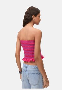 Strapless pink top med smocket tekstur og flæsekant, kombineret med lyseblå jeans, der viser et tætsiddende design.