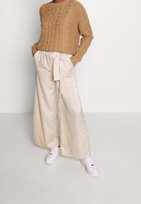 Beige knitted sweater with cable pattern; wide-leg satin trousers tied at the waist; white sneakers. Minimalistic design with neutral colors.