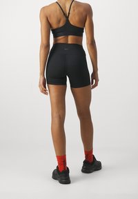 Reggiseno sportivo nero e pantaloncini a vita alta in tessuto morbido; calzini rossi con dettagli neri; scarpe da ginnastica nere; design minimalista.