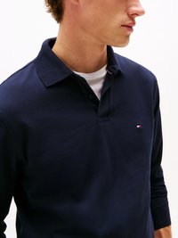 Polo liso azul-marinho com um tecido texturizado, apresentando uma gola e um pequeno logótipo bordado no peito. mangas compridas com punhos canelados.