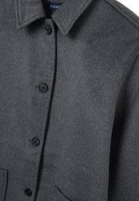 Cappotto grigio in lana con colletto, chiusura frontale con bottoni neri e due tasche laterali. Texture morbida con un design minimale.