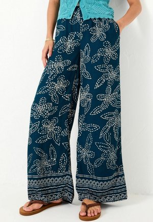 Türkise weit geschnittene Hose mit weißen Blumenmustern, aus strukturiertem Stoff und mit Taschen. Der Saum hat einen gemusterten Rand.
