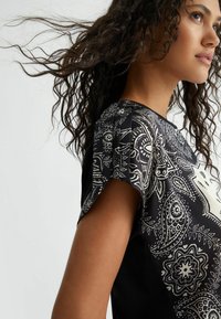 Top nero con motivo paisley bianco, maniche corte, tessuto morbido, vestibilità larga e scollatura rotonda, con pannelli laterali a contrasto.
