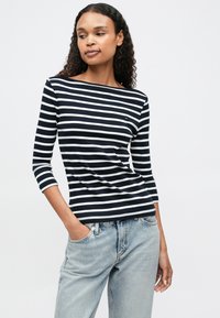 Námořnický a bílý pruhovaný top s dlouhým rukávem a lodním výstřihem, s malým logem. Spárovaný se světle modrými džínami. Měkká textura tkaniny.
