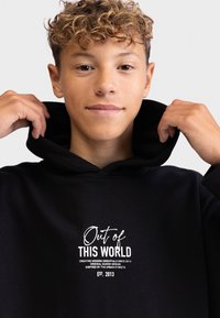 Felpa nera con cappuccio e coulisse, dotata di tasca frontale. Presenta scritte bianche che dicono "Fuori da QUESTO MONDO" e dettagli sul marchio.