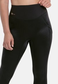 Hochgeschnittene schwarze Leggings mit einem strukturierten Muster, aus elastischem Stoff gefertigt. Verfügt über einen glatten Bund und Seitentaschen.