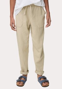 Pantalons en lin beige avec une coupe décontractée, dotés de poches latérales et de ourlets retroussés, associés à des sandales bleues avec deux bandes à boucle.