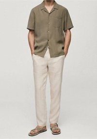 Olijfgroene korte mouwen blouse met knopen, beige linnen broek en bruine sandalen met bandjes. Voorzien van een borstzak en een losse pasvorm.