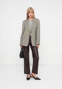 Szary żakiet w wzory, szara bluzka, brązowe spodnie z sztucznej skóry, czarna torebka oraz czarne szpilki. Gładkie białe tło.