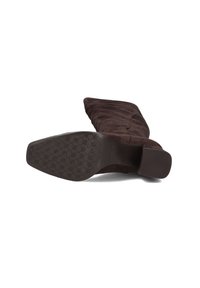 Bruine suede kniehoge laars met een ronde neus, gestructureerde bovenkant en een platte rubberen zool met een honingraatpatroon.