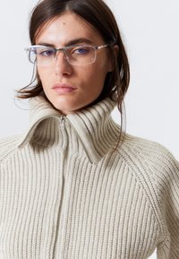 Beiger gerippter Pullover mit hohem Kragen und Reißverschluss. Verfügt über ein strukturiertes Strickmuster und einen kontrastierenden glatten Kragenrand.