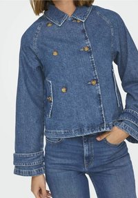 Kurtka dżinsowa ma krótki krój, podwójnie zapinaną konstrukcję, jasnoniebieski kolor, duże guziki oraz dwie przednie kieszenie z kołnierzykiem.