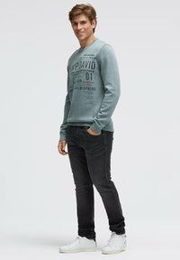 Hellblaues Sweatshirt mit Rundhalsausschnitt und bedruckten Grafiken, kombiniert mit schwarzen Jeans und weißen Turnschuhen, mit schmaler Passform und gerippten Bündchen.