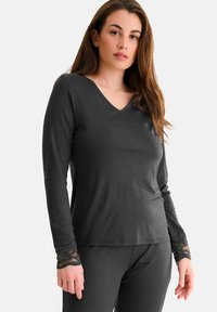 T-shirt à manches longues noir avec un col en V, présentant des accents en dentelle au niveau des poignets. Tissu doux et léger pour plus de confort.